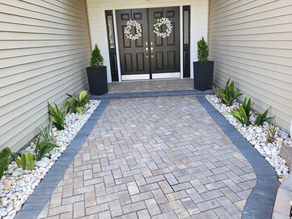 brown front entrance doors to the home with gray and tan Belgard paver stones