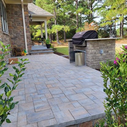 Paver patio behind a brick home with an outdoor paver kitchen and bbq grill