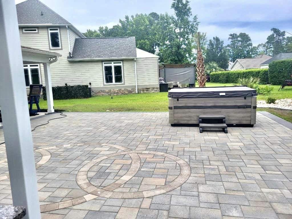 Belgard paver patio with a circle pattern and multi-color paver design in a backyard with a hot tub in the background