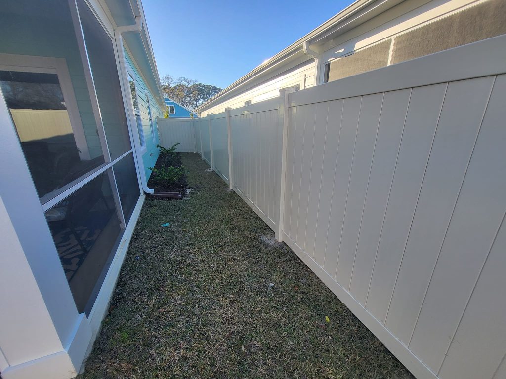 the cream vinyl fence on the right with a house on the left. Very narrow fenced-in yard.