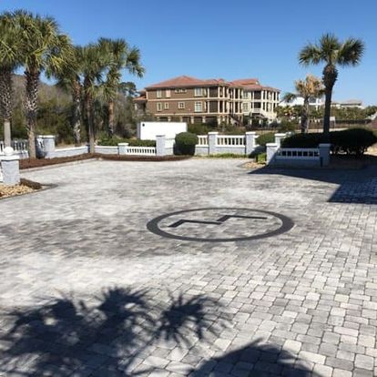gray paver stone driveway with a black monogram in the center and a large home in the background