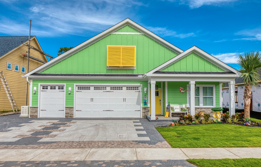 a mix of concrete and brown paver stones on a new driveway with a bright green house in the back of it