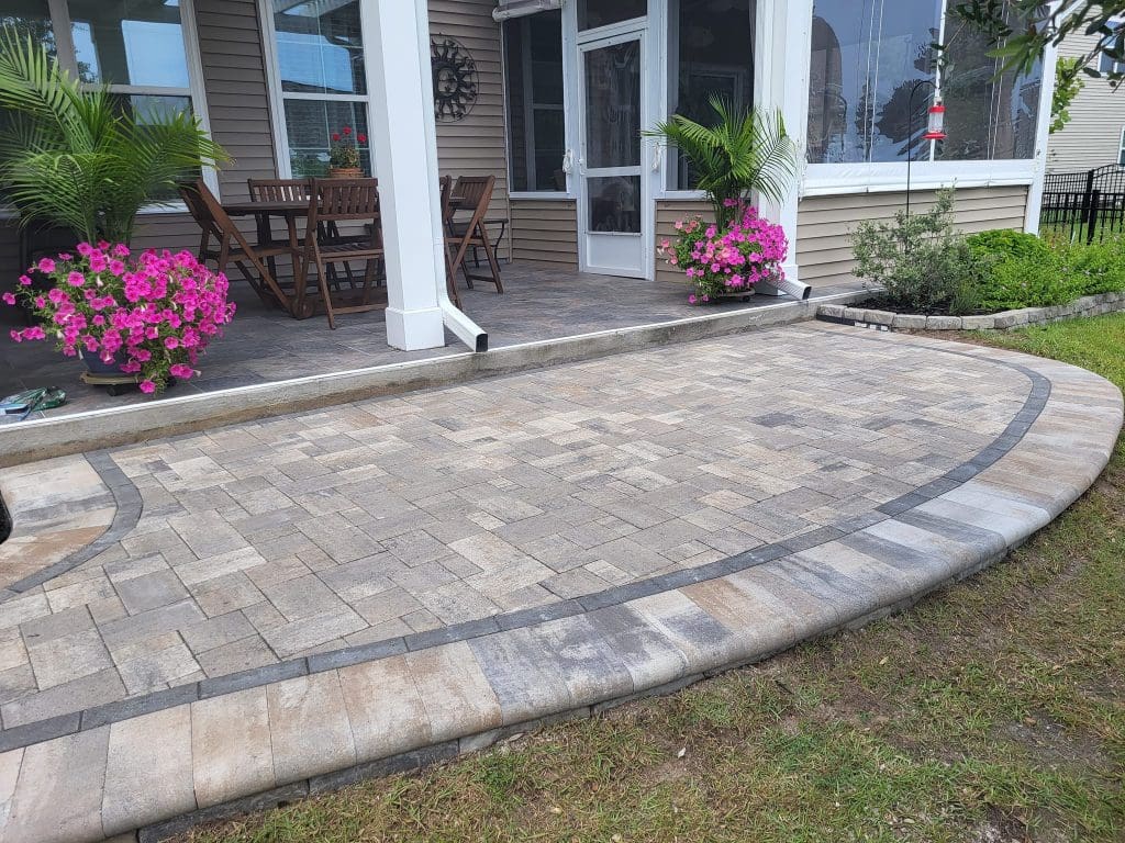 oblong shaped paver stone patio in different shades of brown, tan and gray with a dark line pattern