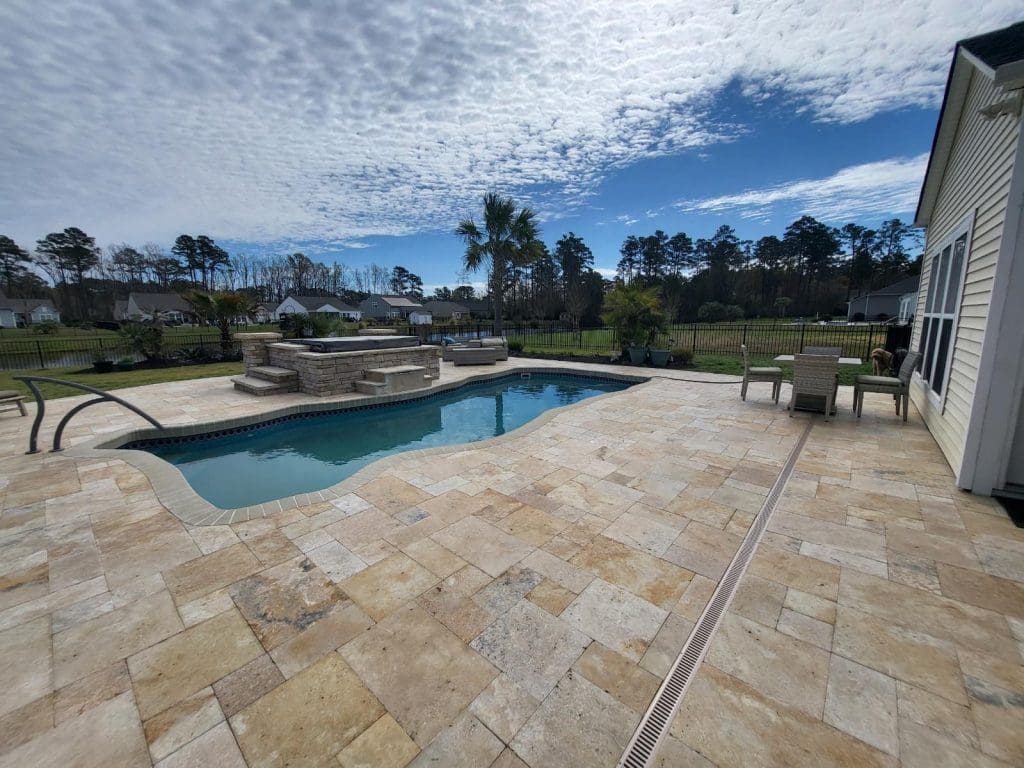 golden yellow and tan large square paver stone patio with a pool and hot tub in the background