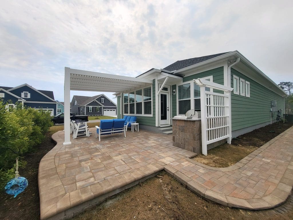 brown and orange raised paver patio with a pergola and walkway around a green house