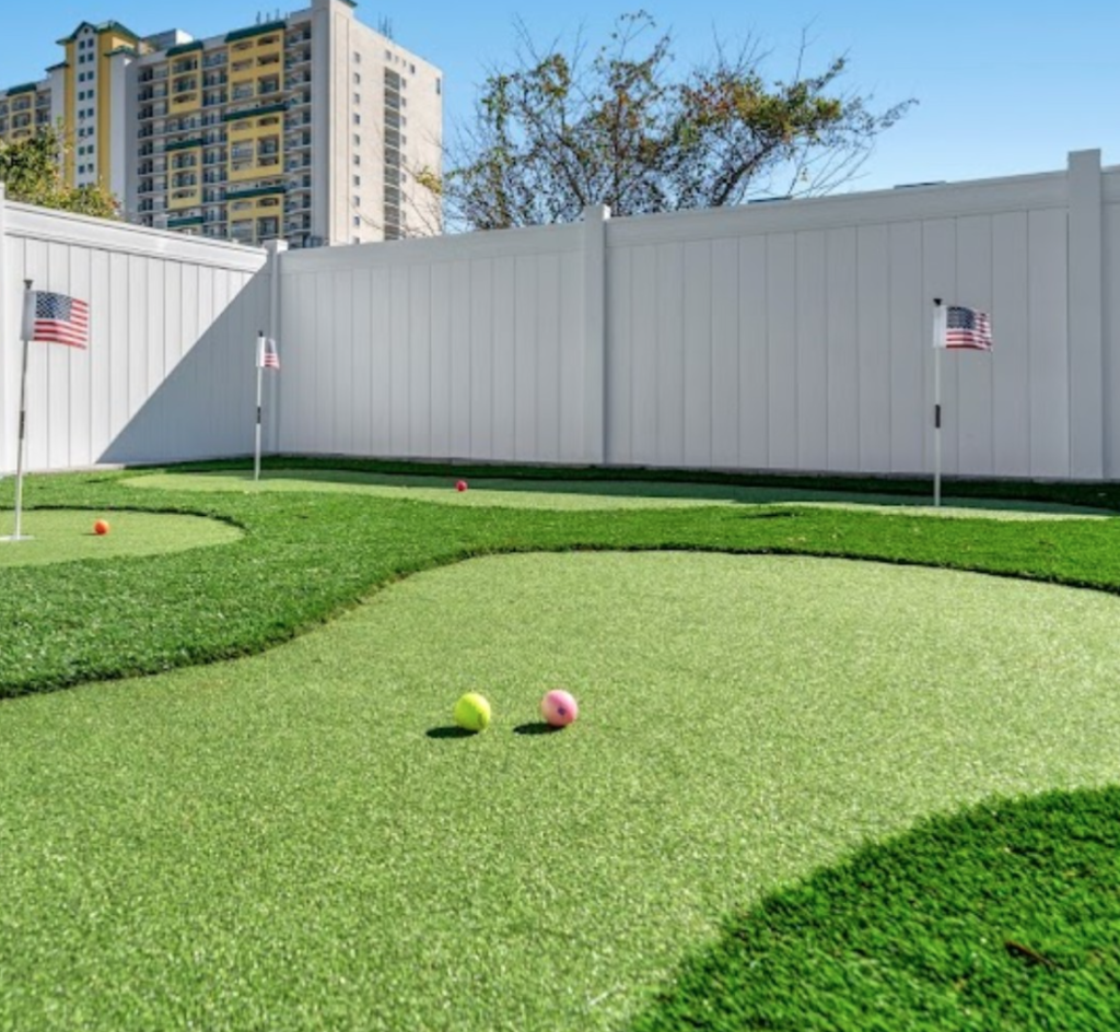 artificial turf putting green installed with a white vinyl fence in myrtle beach by elite coastal landscaping